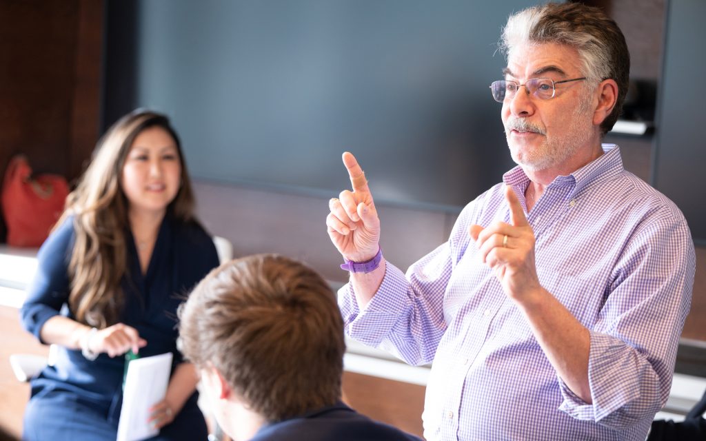 a professor motions with his hands to a room of students