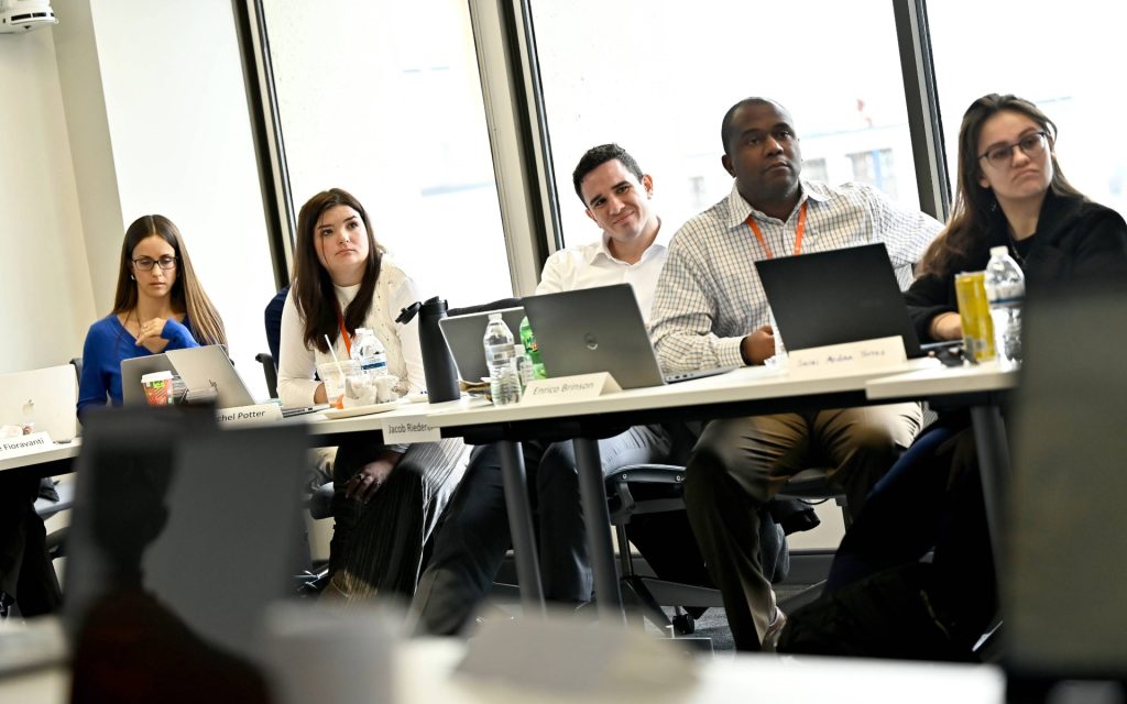 Students sitting at table with laptops looking at front of class. 