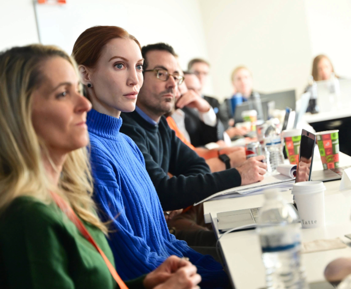 Line of students sitting at table looking at front of class.