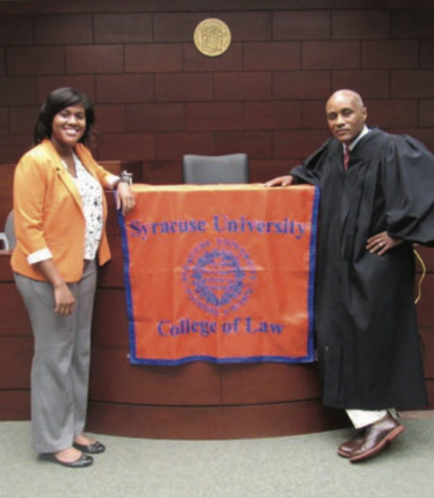 Lishayne King L’18 and Hon. Rodney Thompson L’93, G’93 in courtroom with SU COllege of Law flag