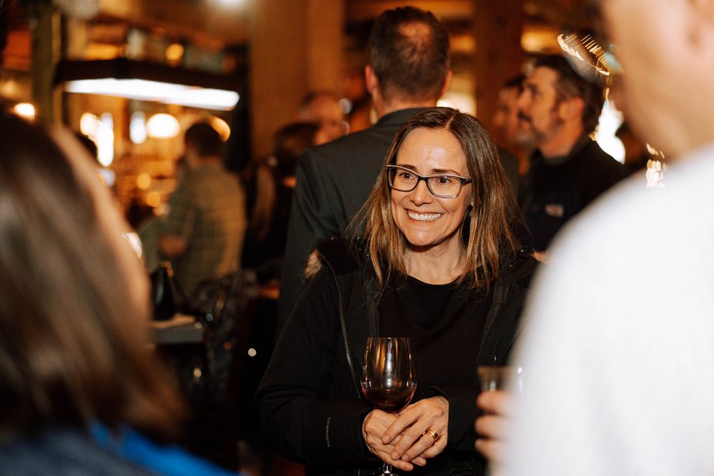 Woman smiles and talks to someone while holding a wine glass