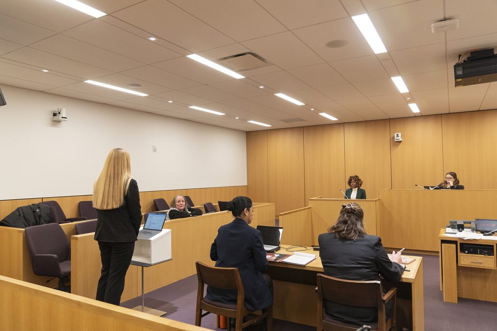 five students sit in the courtroom, practicing trial advocacy, wearing black suits