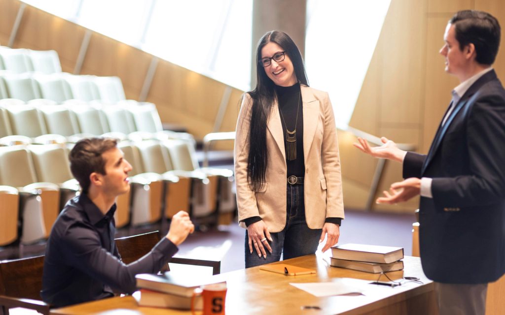 Alison Carlos in courtroom with two fellow students standing around a desk. 