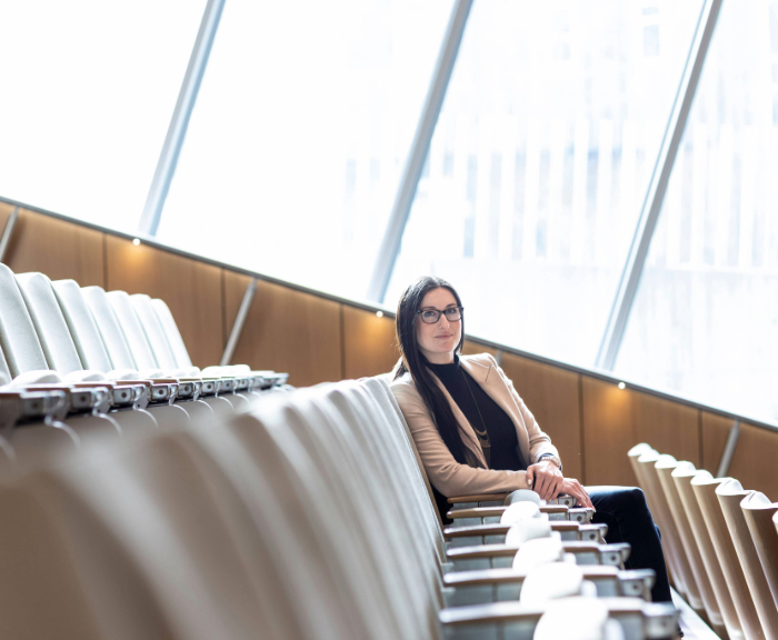 Allison Carlos sitting in courtroom seating with window behind her looking at the camera