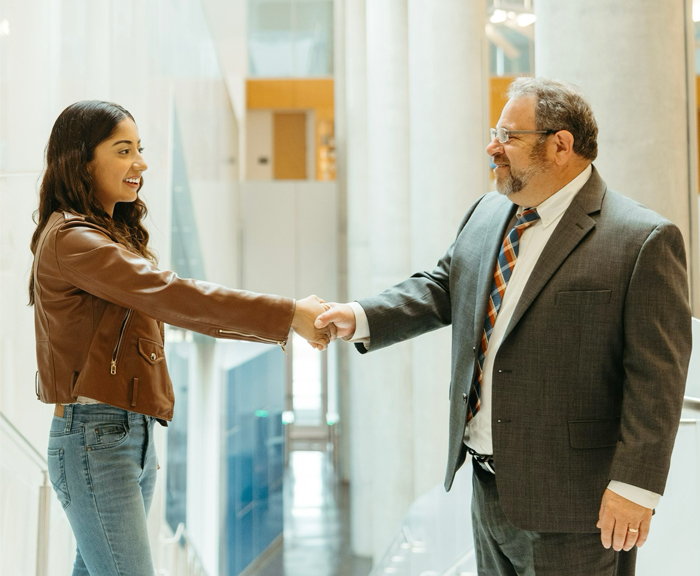 Maheen and Professor Gary Pieples shake hands in the hallway