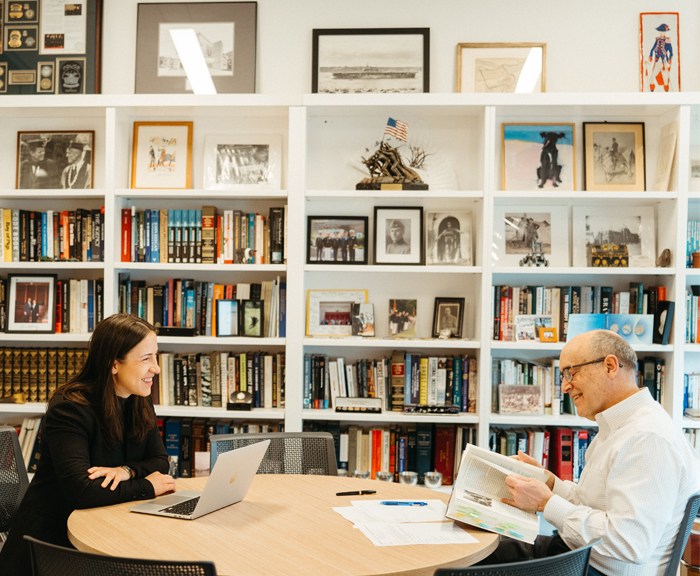 Baker and Cudowska work across a table from each other in front of a bookshelf