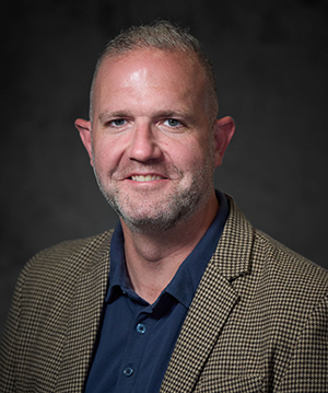 Headshot of Ryan Barker in front of a gray background