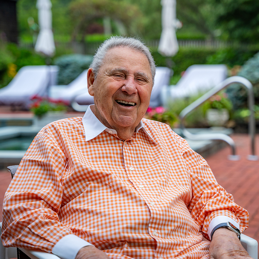 bernard kossar in an orange checkered shirt smiling at the camera sitting outside in his backyard