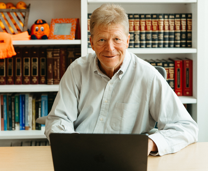 George Boehme looks up from his laptop and smiles. Behind him is a bookshelf.