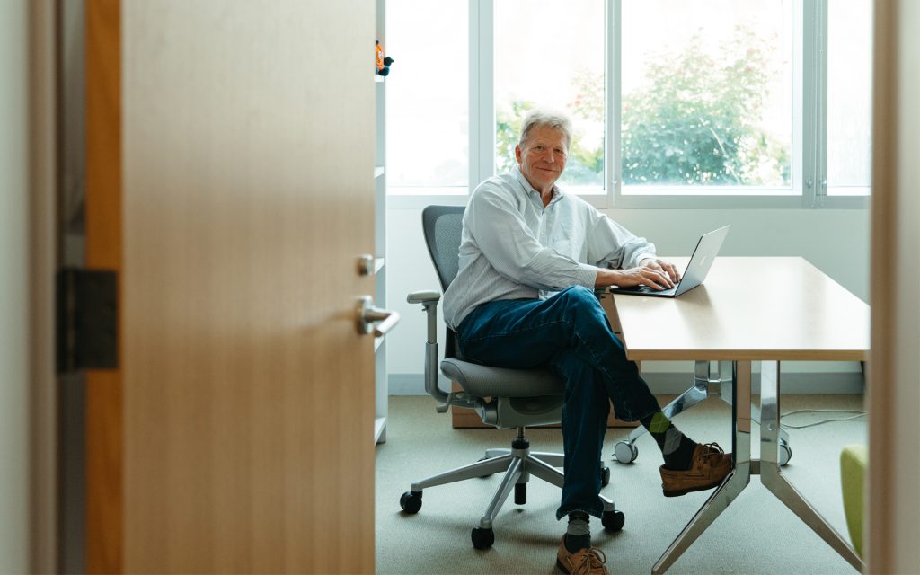 George sits at a desk and looks over through the office's open door