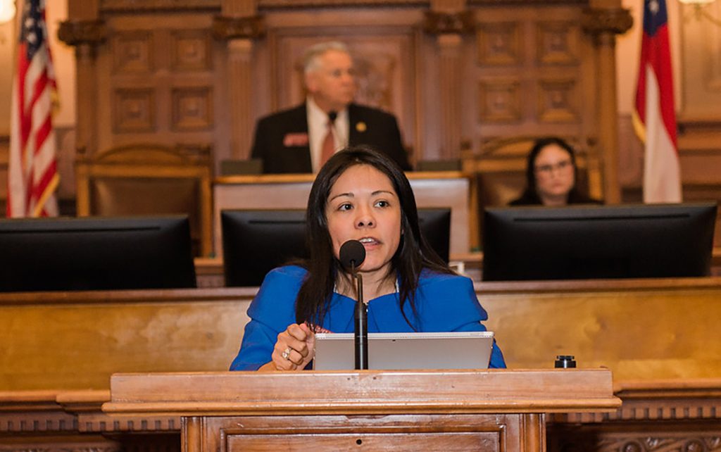 Brenda Lopez Romerez speaks into a microphone at a podium in the courtroom, with two people seated behind her