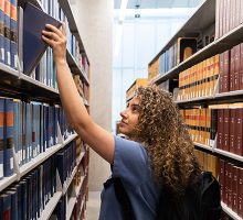 student reaches up to get a book in between a stack of two rows of books in a library
