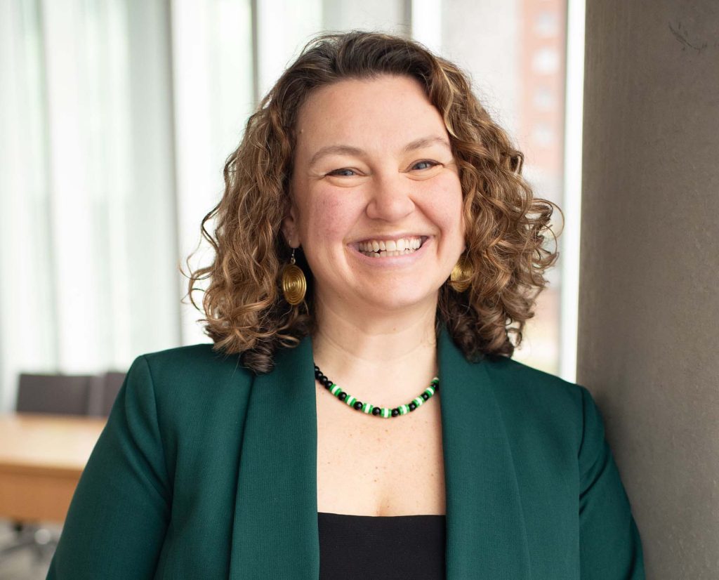 Colleen Gibbons stands in front of a window, wearing a green blazer and a black shirt