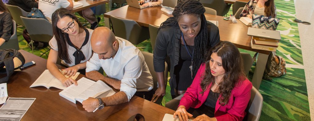 four students work around a table and laptops in the atrium of the college of law