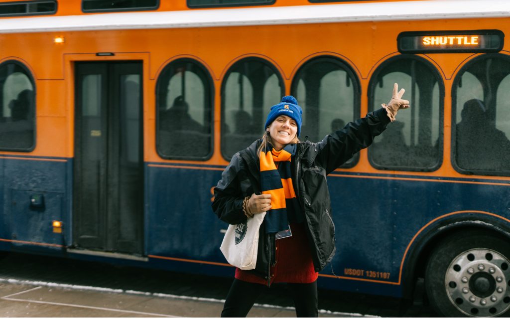 A JDi student poses for a photo in front of a Syracuse University trolley