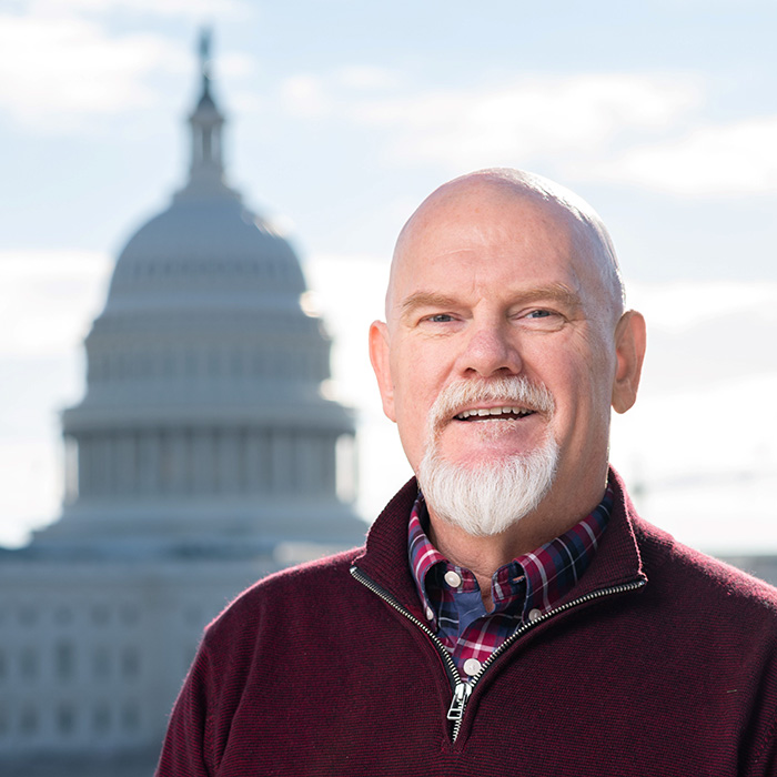Joe di Scipio smiles in front of the US Capitol building outside in a maroon quarter zip