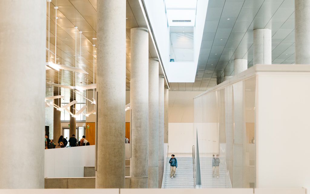 Dineen Hall atrium staircases, with the columns on the left and a student walking down the staircase on the right.