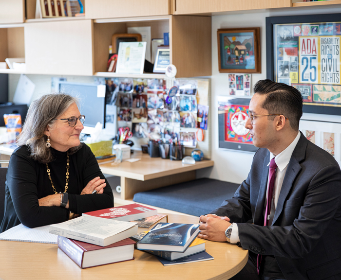 A student meets with a faculty member in their office surrounded by books and art