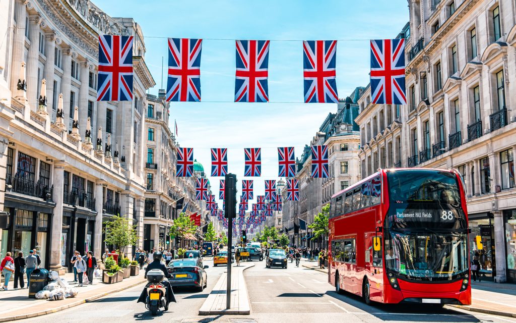 A red double decker bus on a street with British flags hung between the buildings