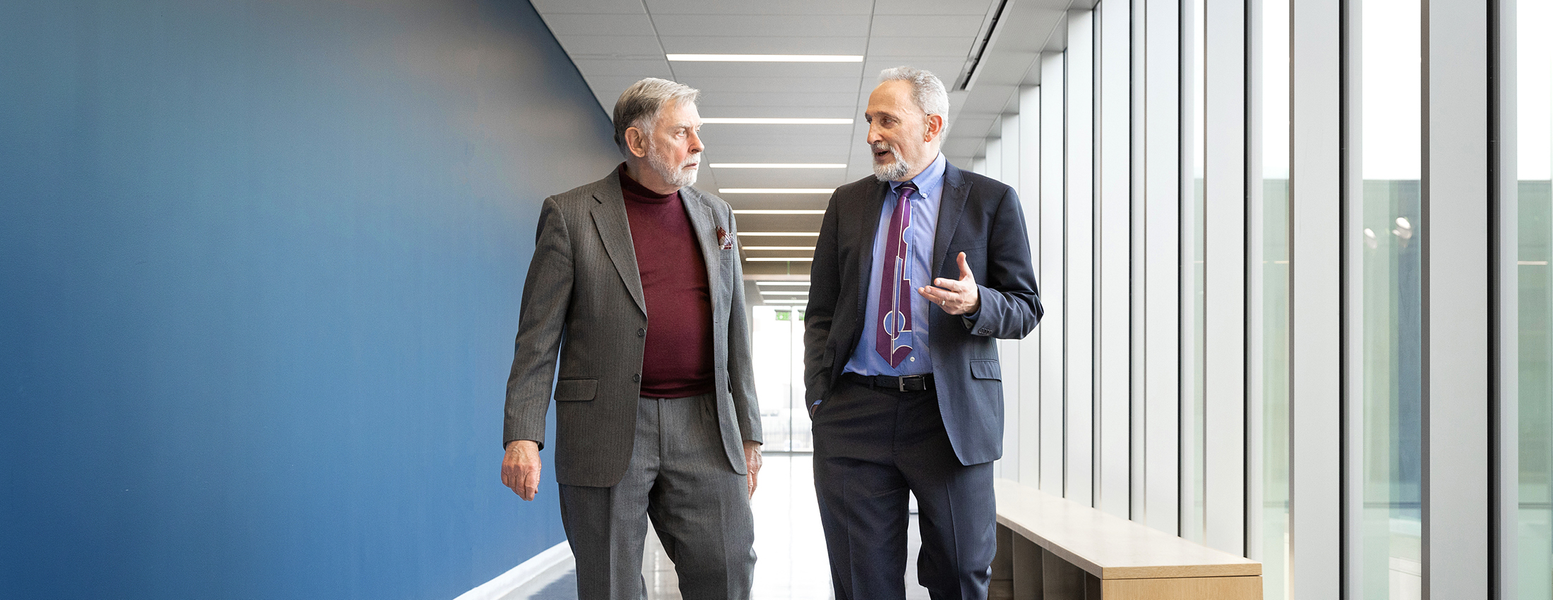 two faculty members walking down the hall facing and talking to each other