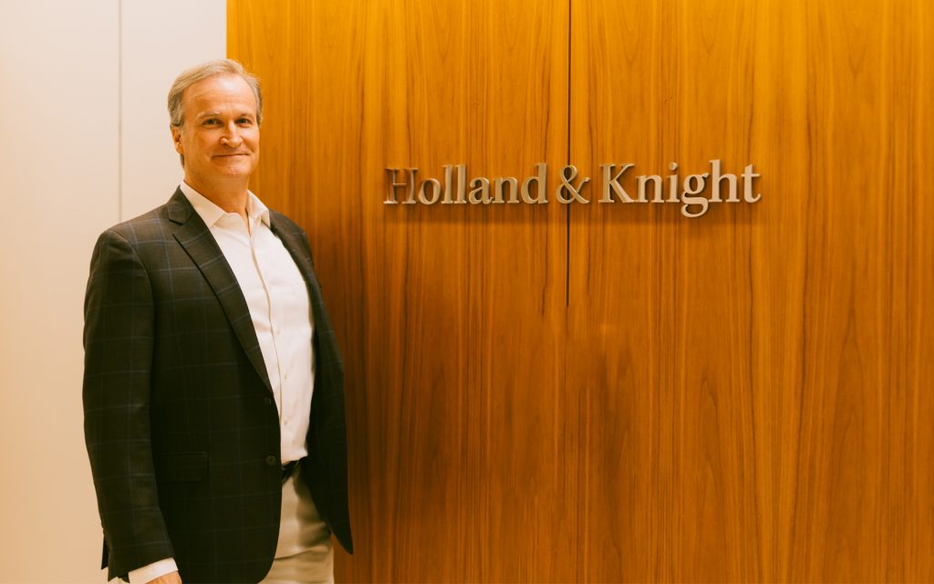 Richard Furey L’94 poses next to the Holland & Knight sign