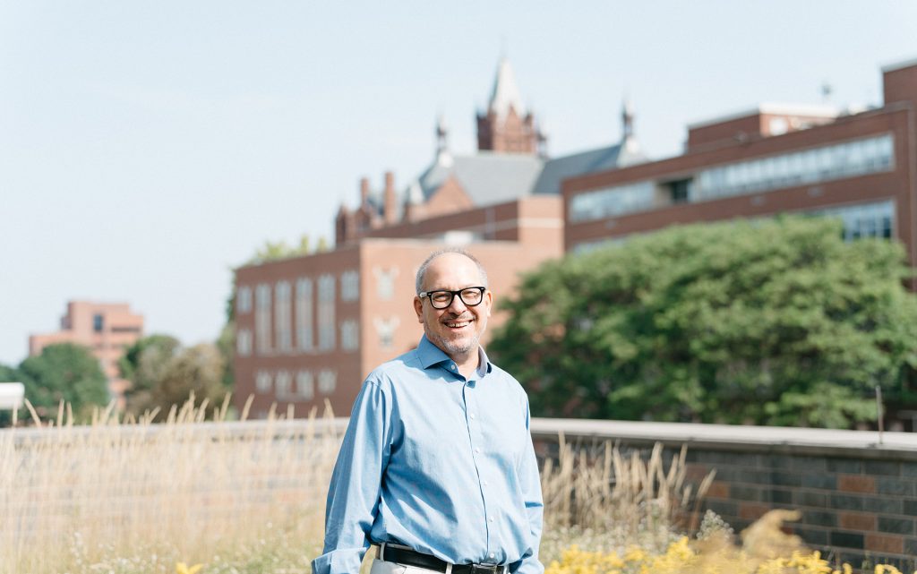 Professor Andrew Greenberg stands outside of the Syracuse College of Law building with grass on the ground.