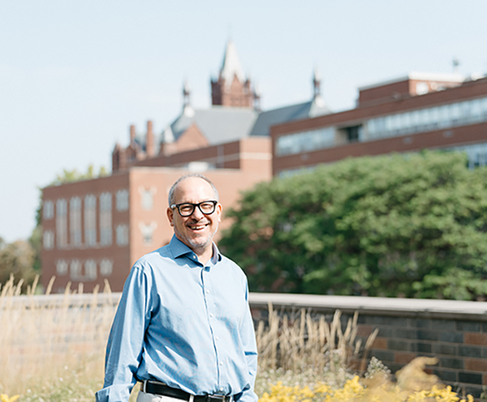 Professor Andrew Greenberg stands outside of the Syracuse College of Law building with grass on the ground.