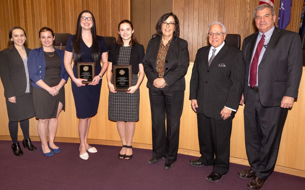 Hon. Thérèse Wiley Dancks L’91 with 6 other people, two holding plaques. Standing in front of Judges bench.