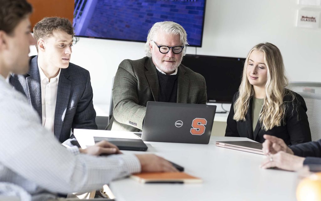 A professor and two students look at a laptop and collaborate in the Innovation Law Center