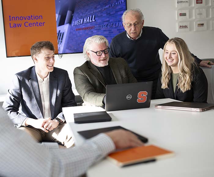 Two professors and two students look at a laptop and collaborate in the Innovation Law Center
