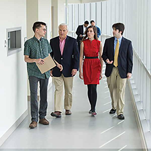 three students walk down a white hallway with a professor, discussing their class
