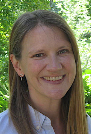 Professor Jennifer Breen, a white woman with dirty-blonde, shoulder-length hair, wearing a white blouse with small, silver earrings, smiles outside.