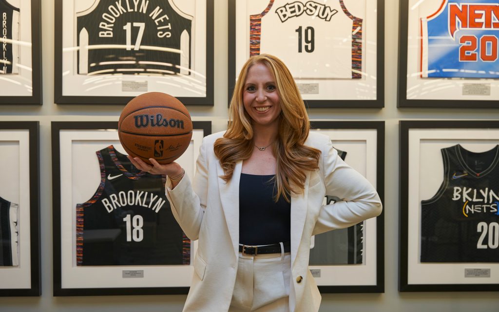 Dana holds a basketball in front of a wall of framed jerseys