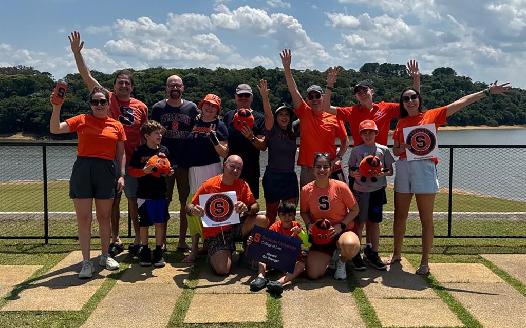 Group of LL.M. students in Brazil stand together for a photo with orange shirts on and various Syracuse Law swag