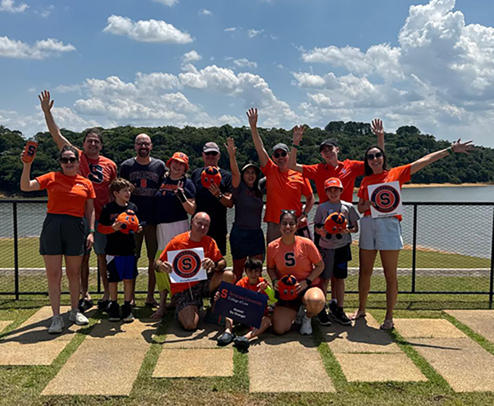 Group of LL.M. students in Brazil stand together for a photo with orange shirts on and various Syracuse Law swag