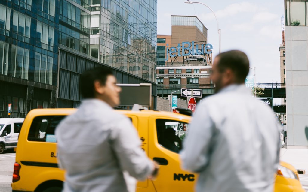 Students wait to cross the road in NYC as a taxi drives by