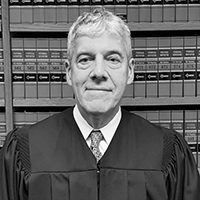 judge stewart aaron in a black and white photo in front of stacks of books at the library, wearing his judge's robe