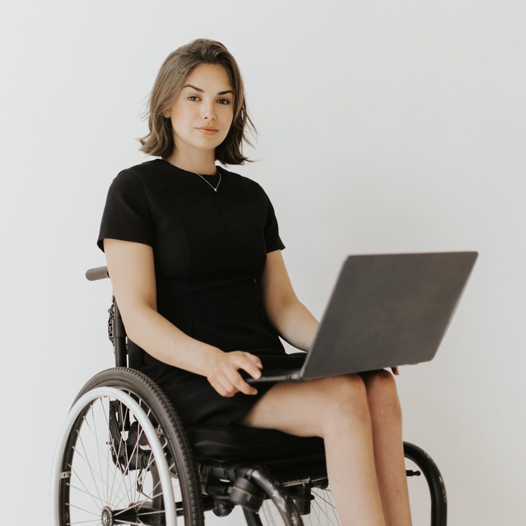 Kaitlin Sommer sitting in wheelchair holding a laptop. 