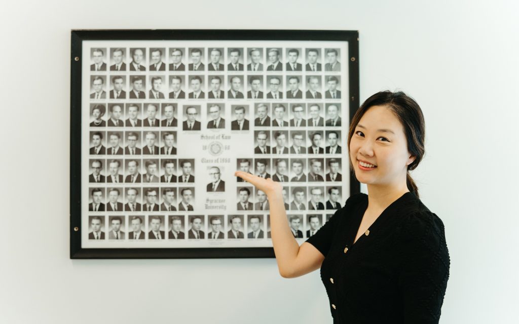 Erica stands in front of at composite of headshots from an alumni class