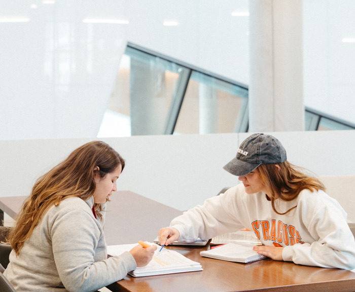 Two female students work together at a table in a brightly lit room.