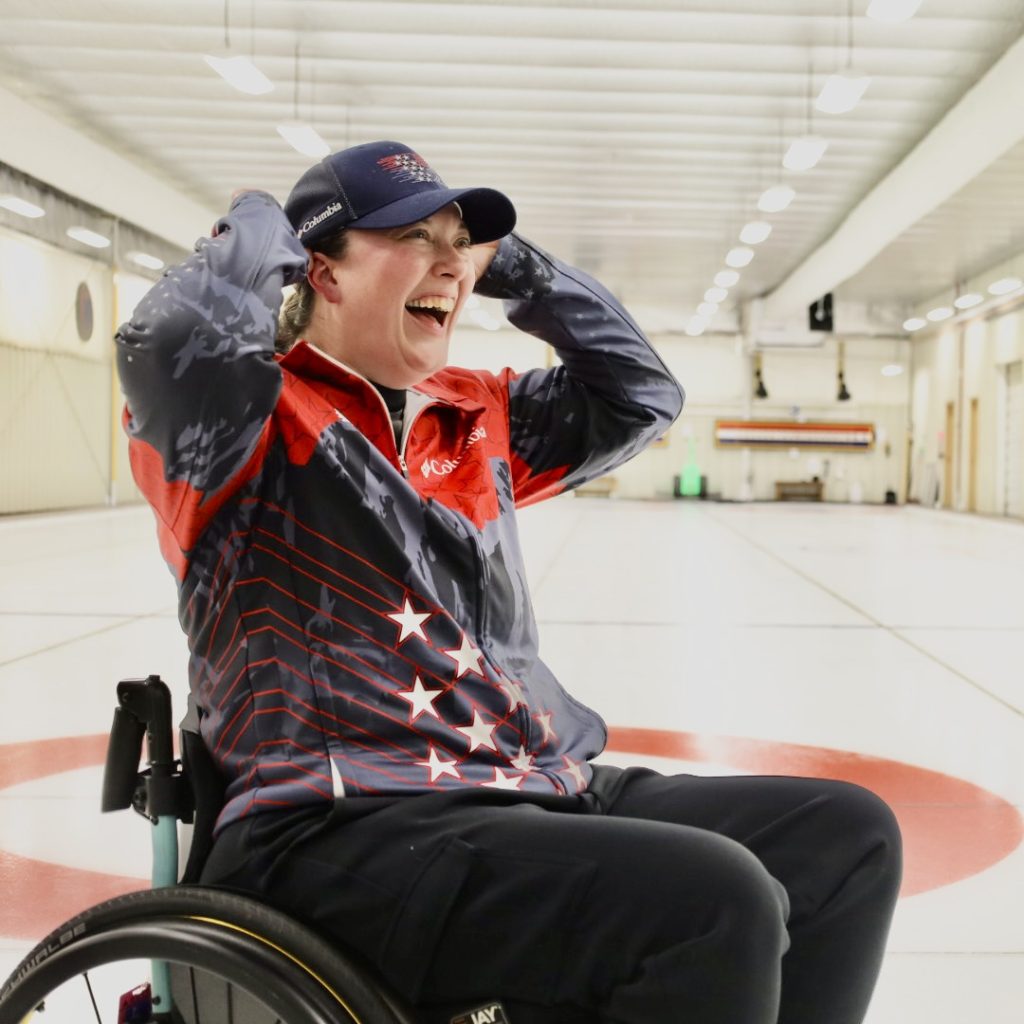 Katie Verderber sitting in wheelchair on ice rink wearing TEAM USA jacket.