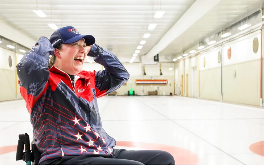 Katie Verderber sitting in wheelchair on ice rink wearing TEAM USA jacket.
