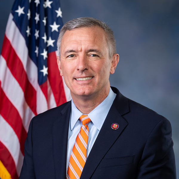 john katko smiling at the camera in a blue suit and orange tie in front of the american flag