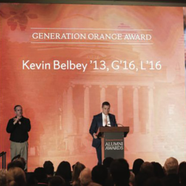 kevin belbey speaking at a podium in front of a orange screen for the generation orange award at syracuse university