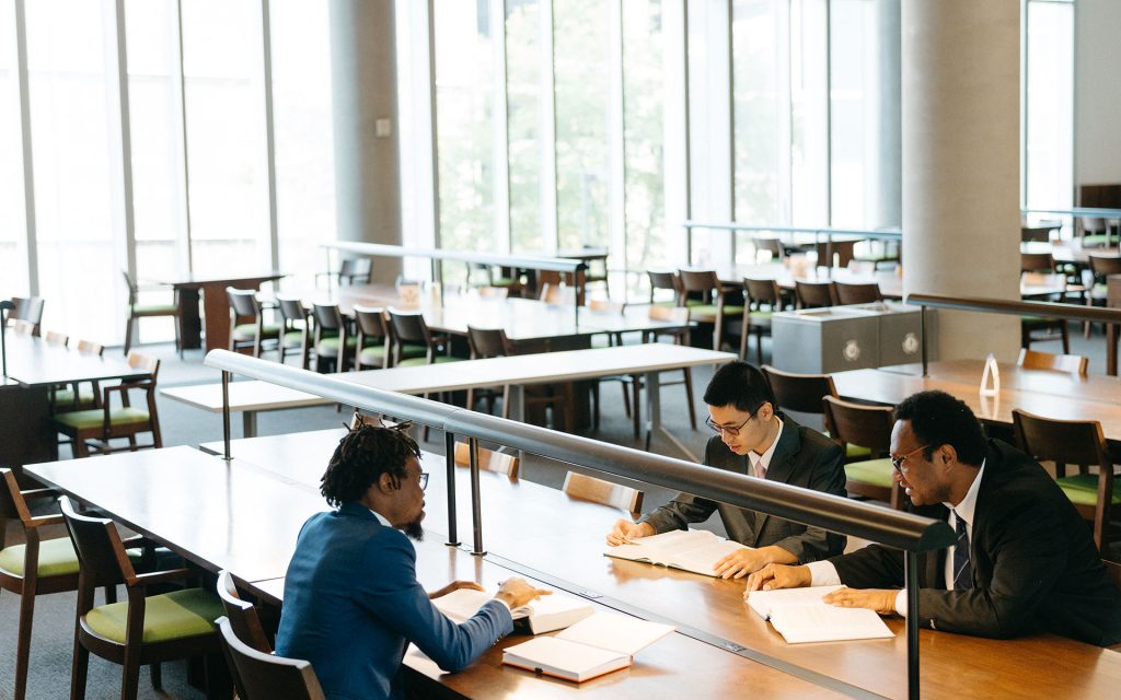 three students work at a desk in the library with papers on the table in front of them