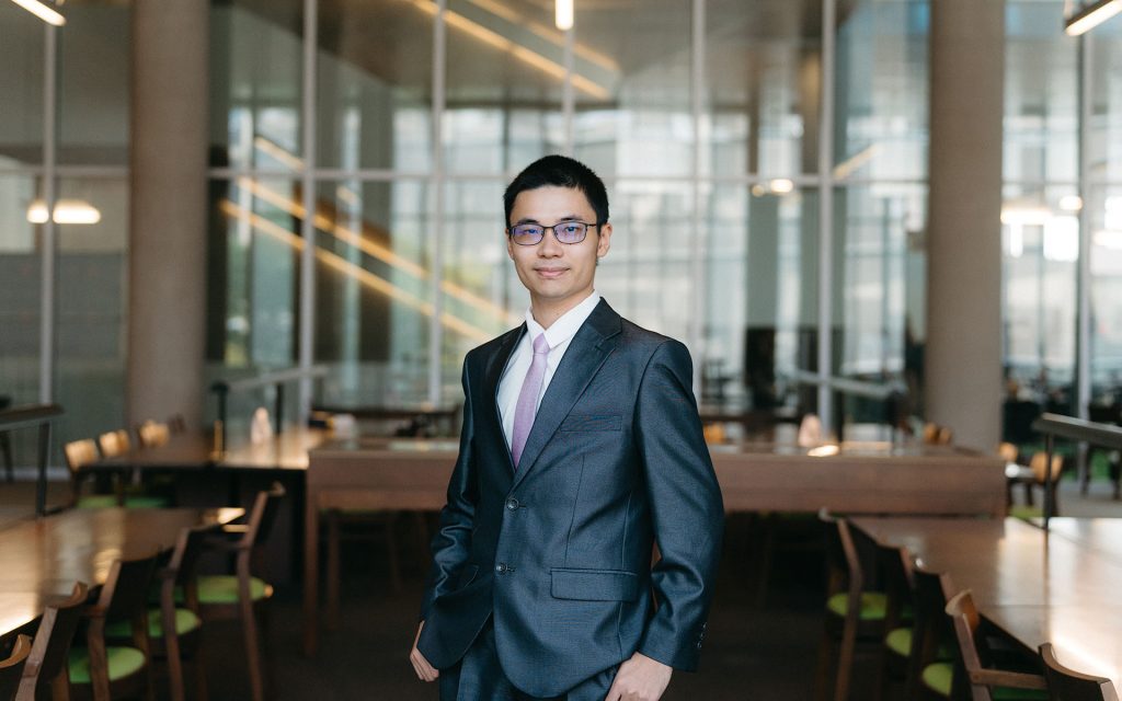 Carr Lin stands in the Syracuse Law library looking at the camera, surrounded by study desks