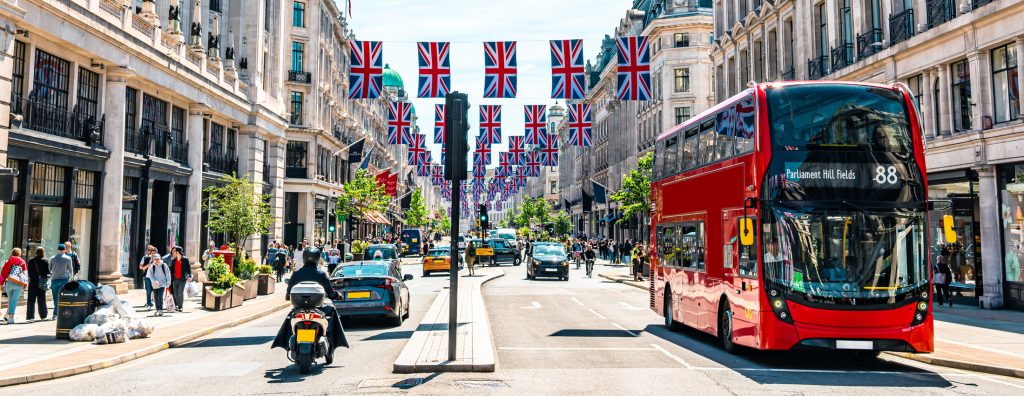A red double decker bus on a street with British flags hung between the buildings