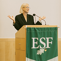 joanie mahoney speaks at a podium in front of an ESF banner, holding her hands out to the sides