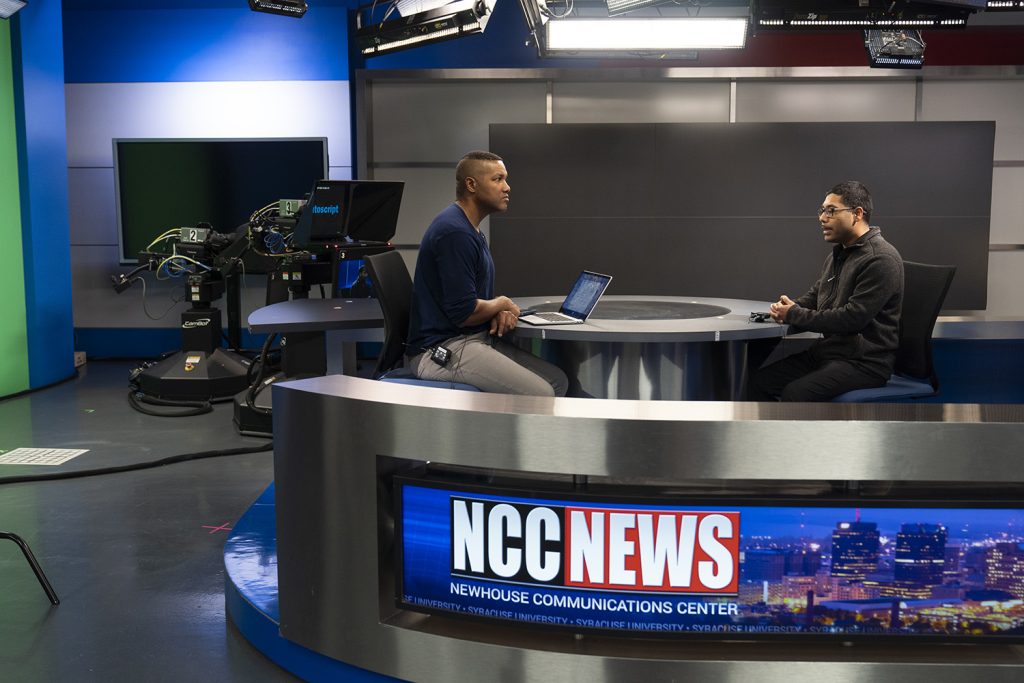 two people talk to each other at a news station for the newhouse communications center