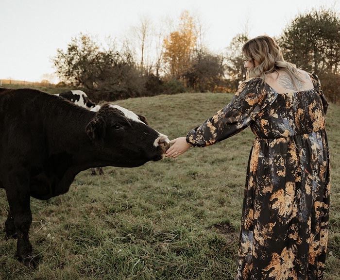 Megan Poole feeds a cow in a field, wearing a floral black dress